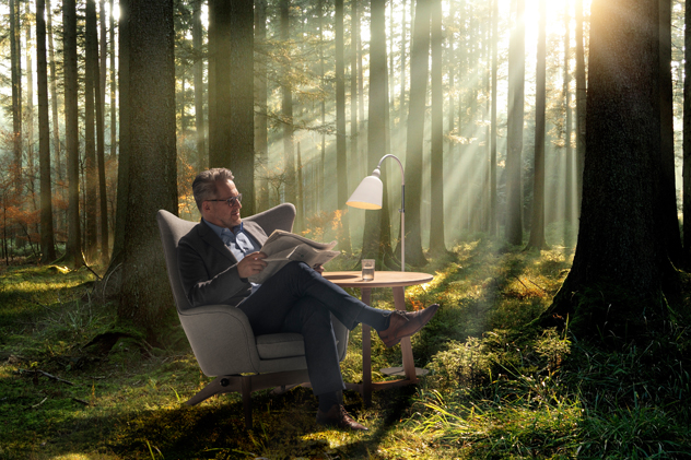 Zeitung lesender Herr im Ohrensessel im Wald.